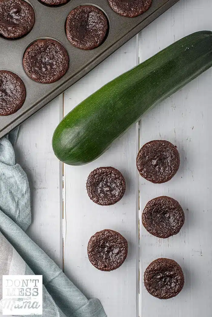 mini zucchini chocolate muffins on a table next to a zucchini and muffin pan