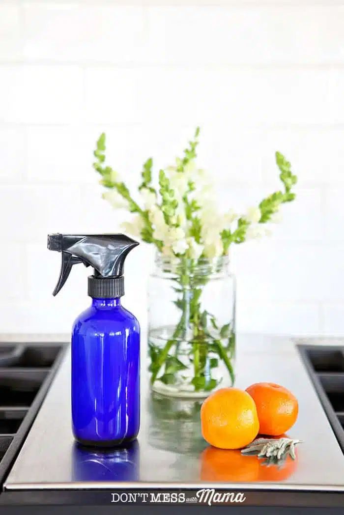 Closeup of glass cleaner, vase of flowers, and oranges on a stovetop