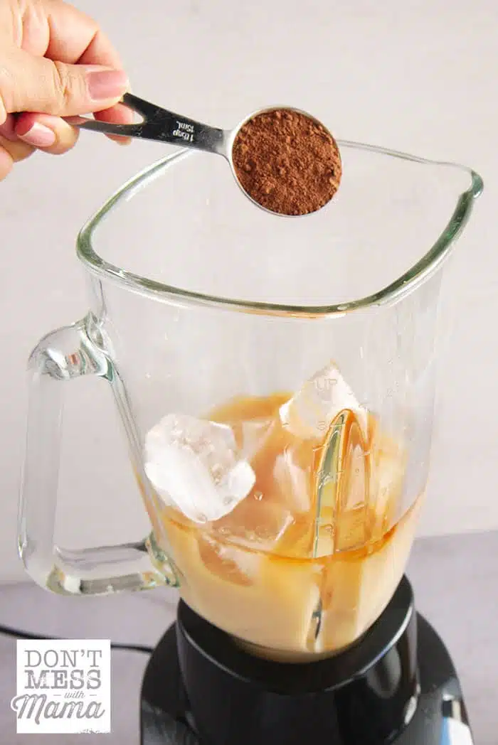 Adding cocoa powder to a blender to make iced coffee