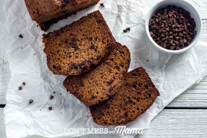 banana bread on parchment paper next to a bowl of chocolate chips