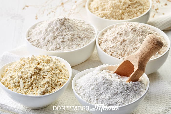 Closeup of five bowls filled with various types of gluten free flours and a wooden spoon