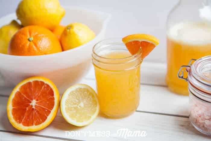 A photo of an orange homemade electrolyte drink in a glass jar on a wooden surface