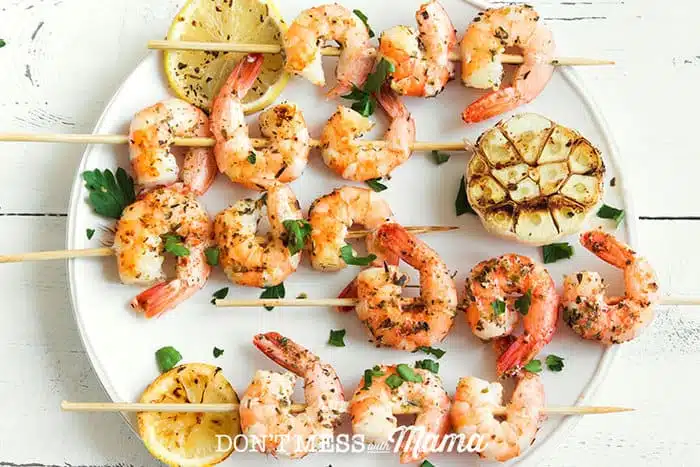 An overhead shot of Lemon Garlic Shrimp Skewers on a white round plate with lemon slices
