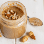 homemade almond butter in a glass gar on a white table with a spoon nearby