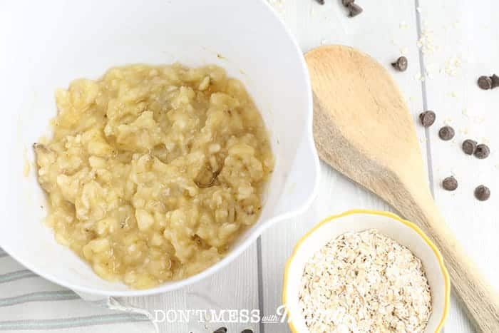 mashed bananas in a white bowl on a table next to a bowl of oats