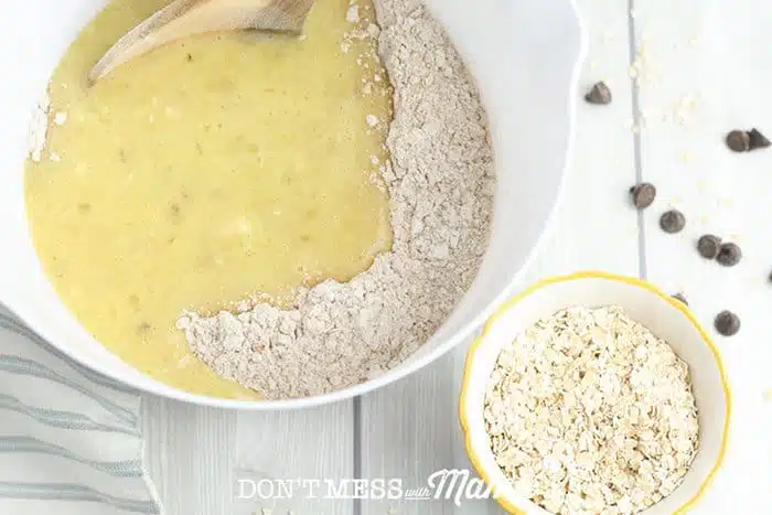 adding beaten eggs to a bowl of flour and oats on a table