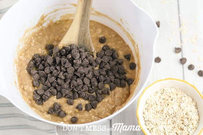 adding chocolate chips to a muffin dough mix in a white bowl