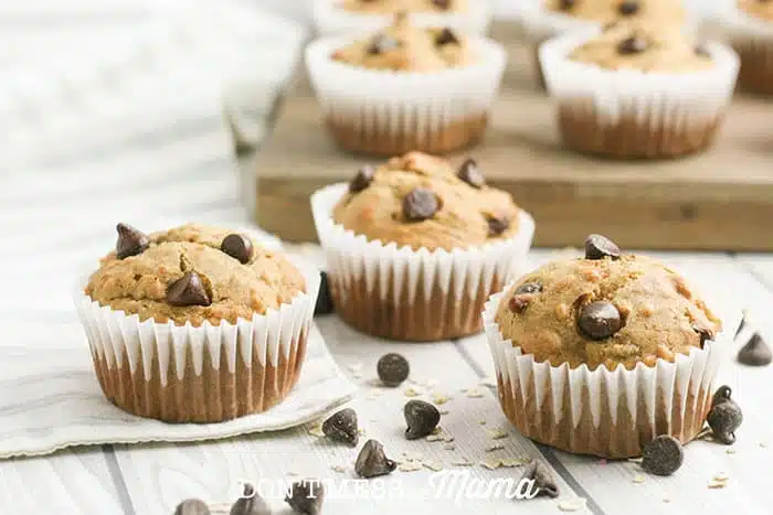 banana chocolate chip muffins on a white table with chocolate chips sprinkled around them