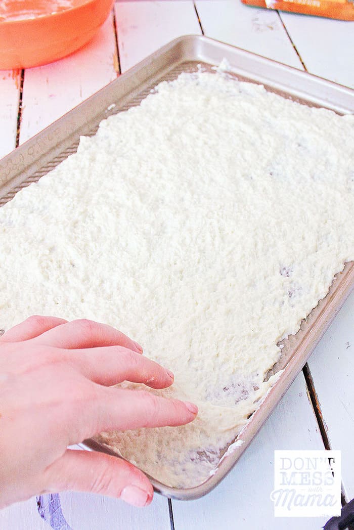 hands rolling out gluten-free pizza dough on a sheet pan