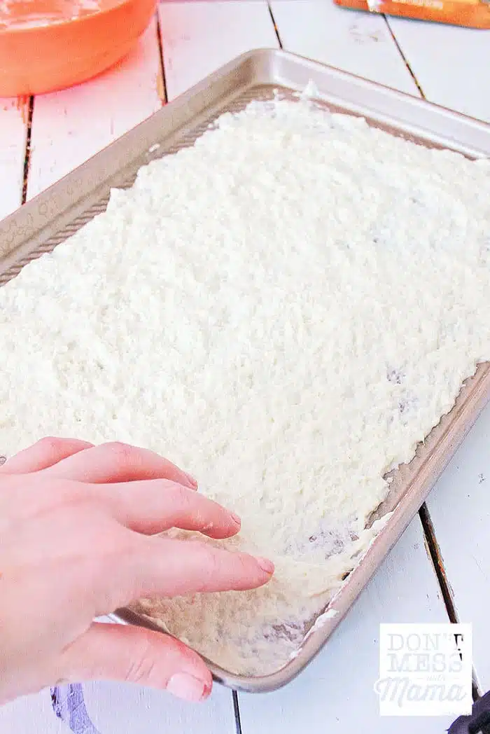 hands rolling out gluten-free pizza dough on a sheet pan