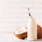 coconut milk in a glass bottle next to an open coconut on a table