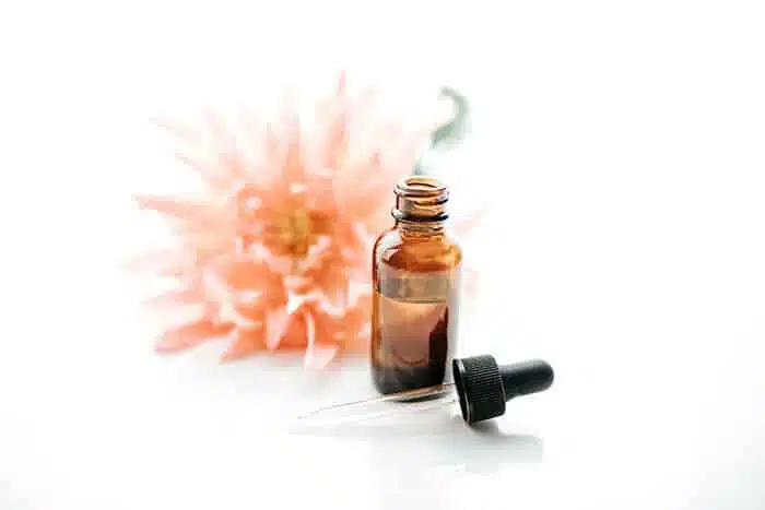 Closeup of DIY argan hair oil serum in a glass bottle with a flower in the background