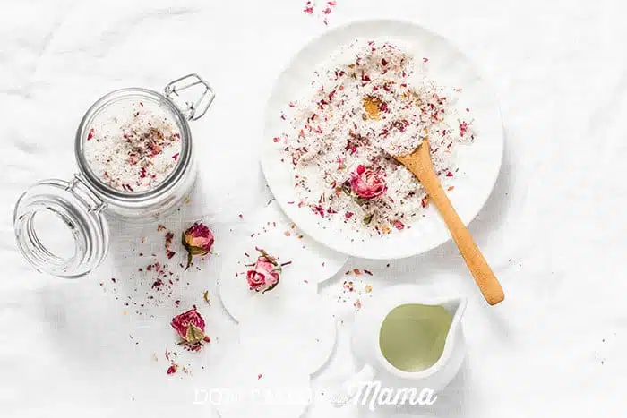 Closeup of homemade bath salts with rose petals in a bowl with a wooden spoon