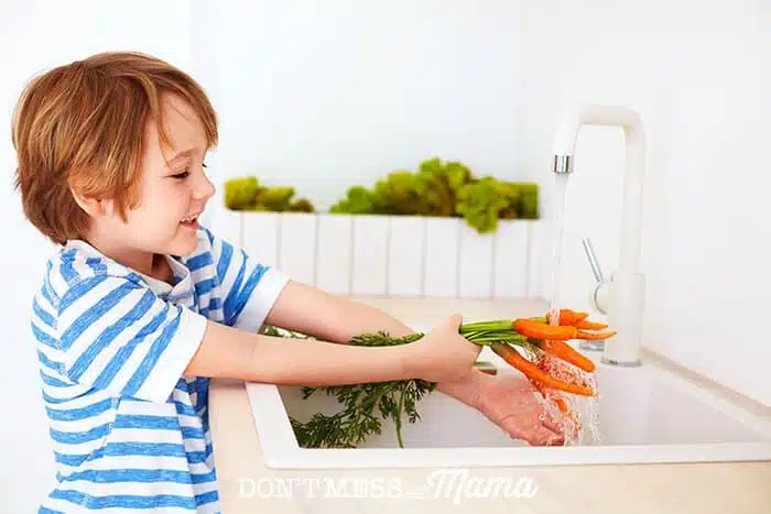 Young boy washing carrots at the sink