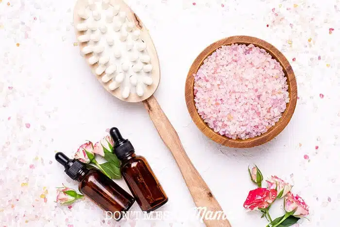 Closeup of essential oil bottles, body brush and bath salts with flowers in the background