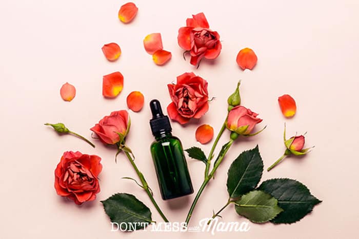Closeup of rose petals on a pink background with a bottle of massage oil