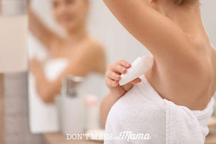 woman putting on deodorant in front of mirror