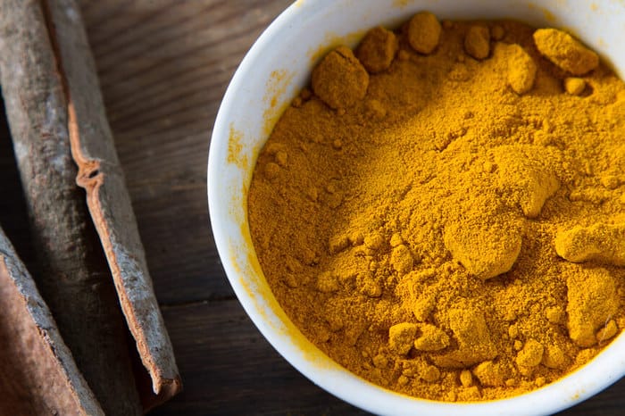 A photo of ground turmeric in a white bowl on a wooden surface and 5 Reasons to Eat Tumeric