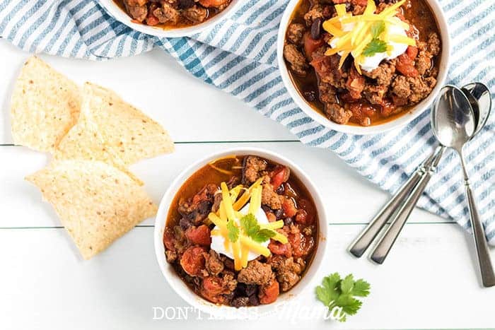 Photo of Instant Pot Beef Chili in bowls with spoons and tortilla chips in the background