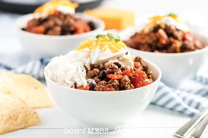  Instant Pot Beef Chili in bowls with rice and tortilla chips in the background