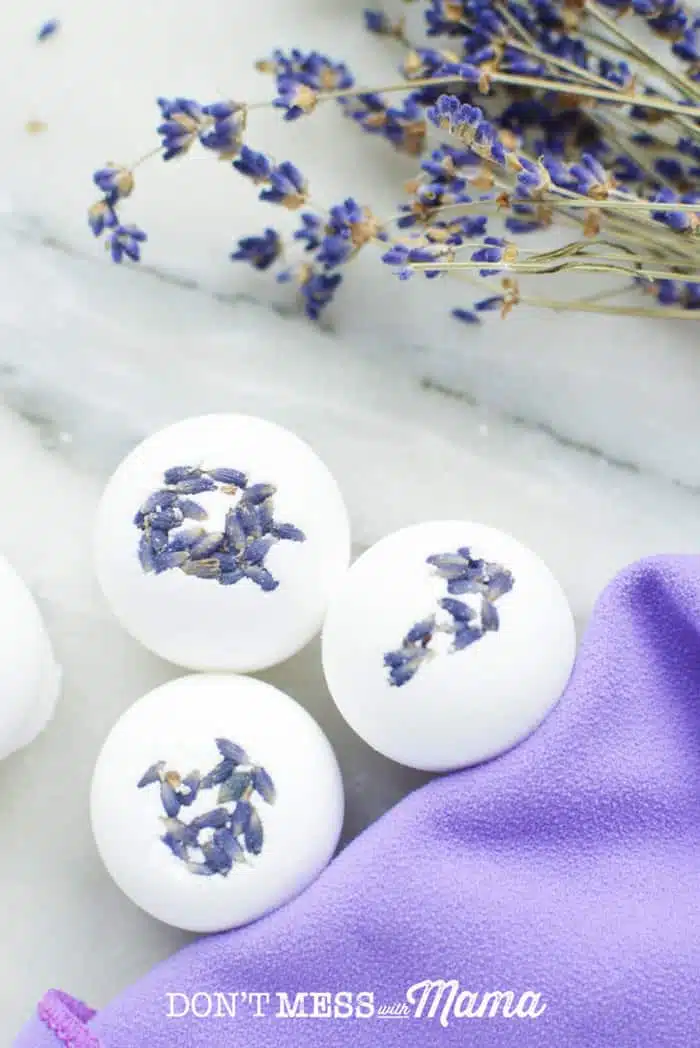 A close up of homemade bath bombs on a white surface with lavendar flowers