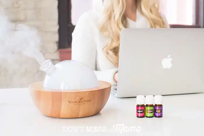 Diffuser on a desk with essential oils and a woman with a laptop working