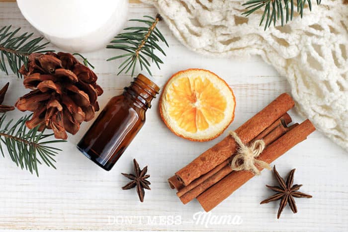 A bottle of essential oils and a cinnamon stick, slice or orange and spices on a wooden surface