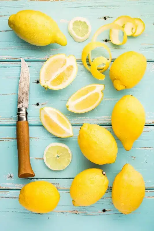 An overhead shot of whole lemons and cut lemons on a blue wooden surface