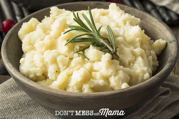 Closeup of mashed potatoes in a bowl with a sprig of rosemary