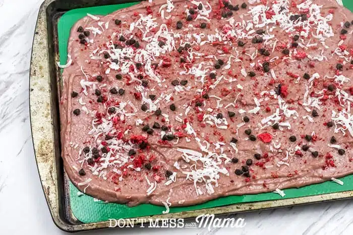 Closeup of strawberry bark spread out on a cookie sheet and topped with chocolate chips and dried coconut 
