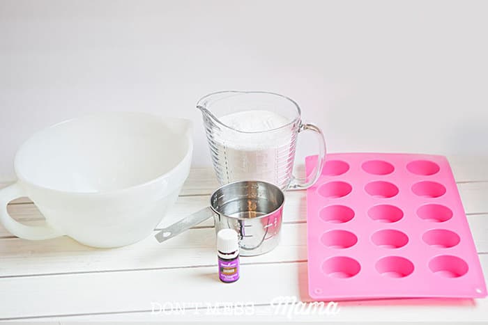 Closeup of mixing bowl, measuring cup, cup of baking soda, lavender oil and silicone mold