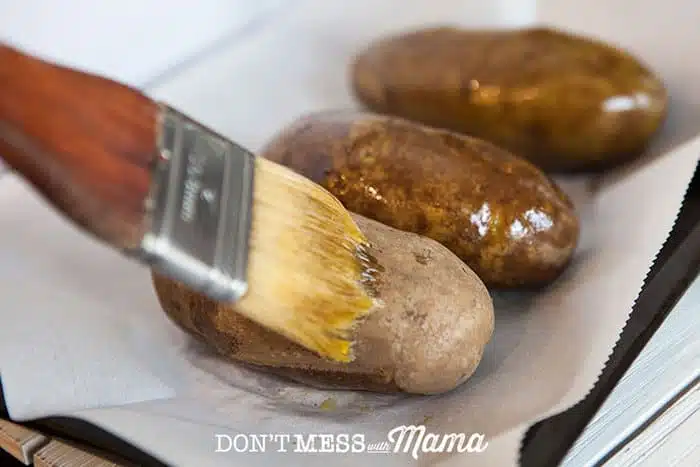 Brushing baked potatoes with olive oil to go into an oven