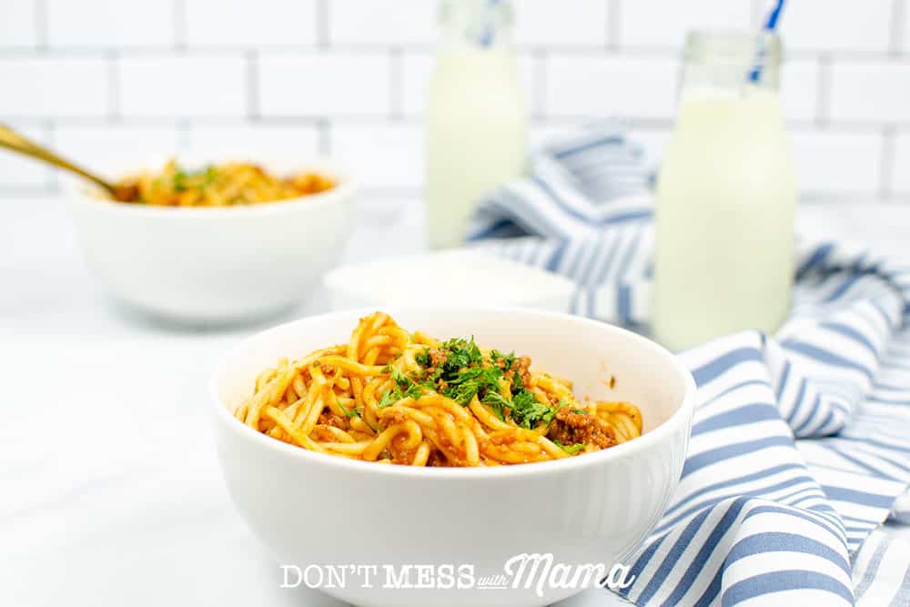Two bowls with spaghetti topped with parsley on a table top with a blue/white towel