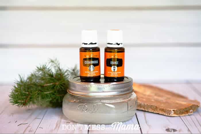 Photo of Cedarwood and Orange essential oils on top of a jar of DIY shave gel with a branch of pine in the background