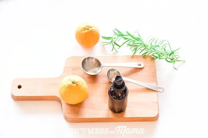 Closeup of DIY dry shampoo spray with oranges and rosemary on a cutting board