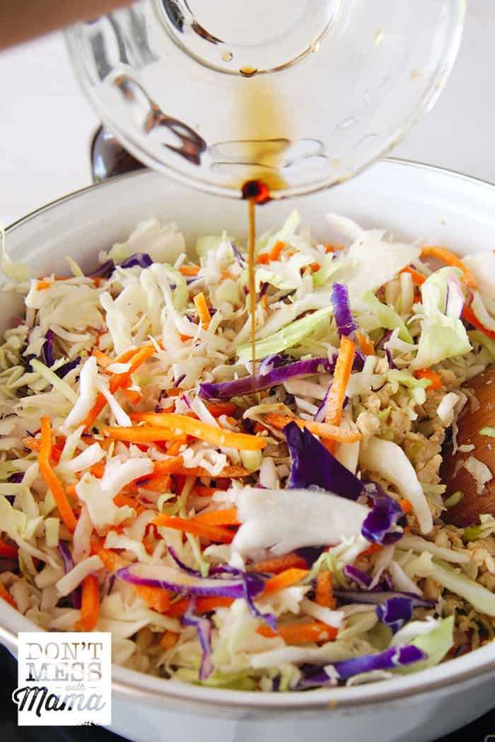 adding gluten-free soy sauce to a pot with shredded cabbage and ground chicken