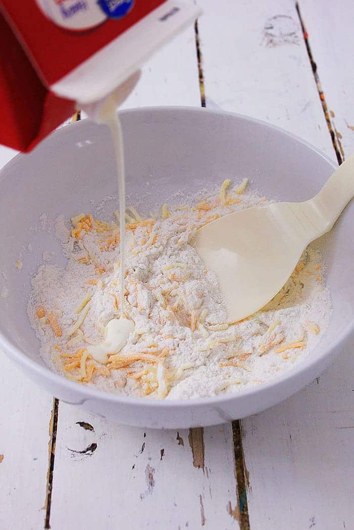adding half and half to a bowl of flour and cheese