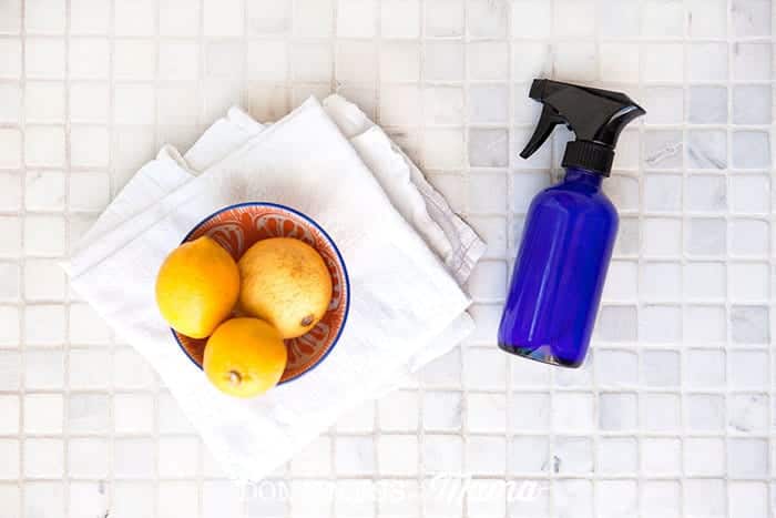 blue glass spray bottle in a shower next to a towel and bowl of lemons