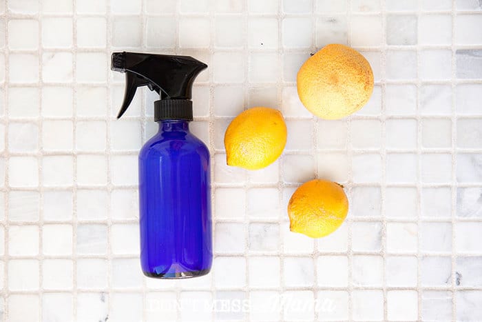 blue glass spray bottle in a shower next to a bunch of lemons