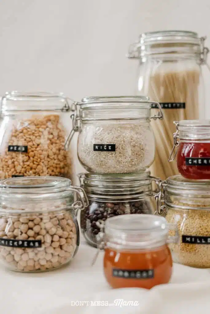 glass jars filled with dry food like beans, rice stacked in a pantry