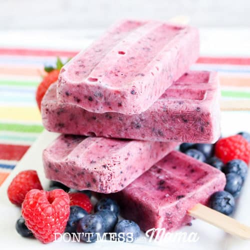 four mixed berry popsicles stacked on plate with berries