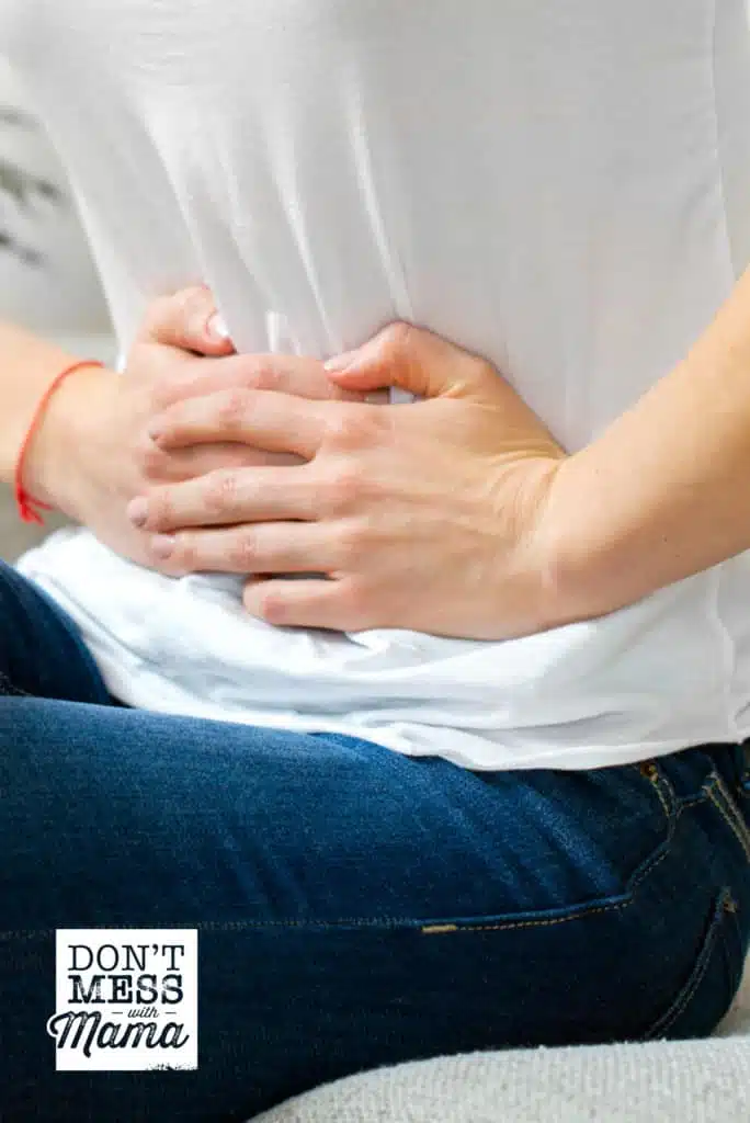 woman holding stomach in pain wearing white t shirt