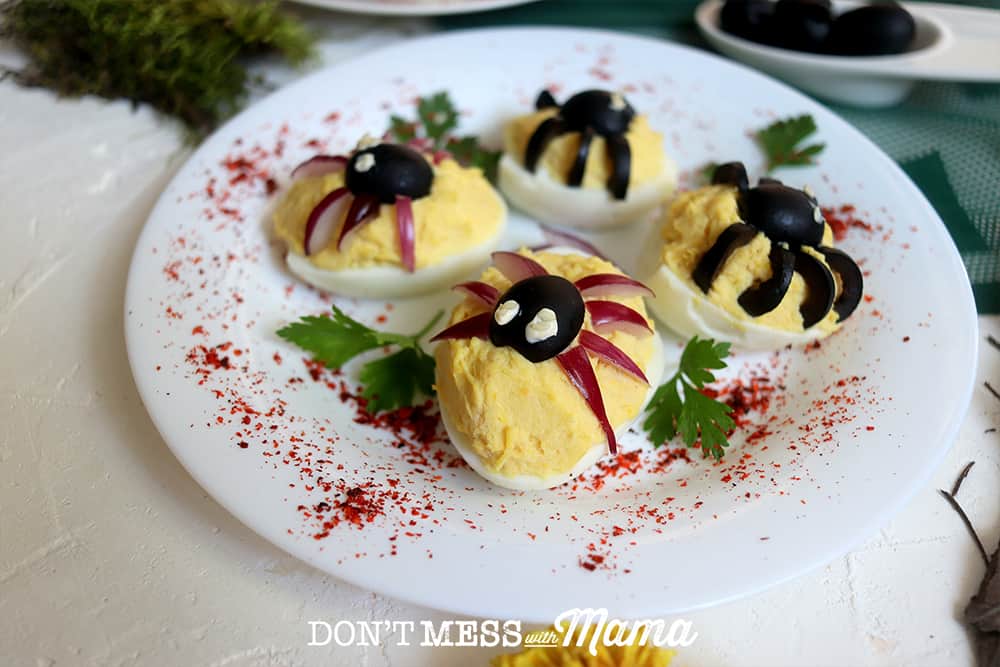 deviled eggs topped with olive spiders on a white plate