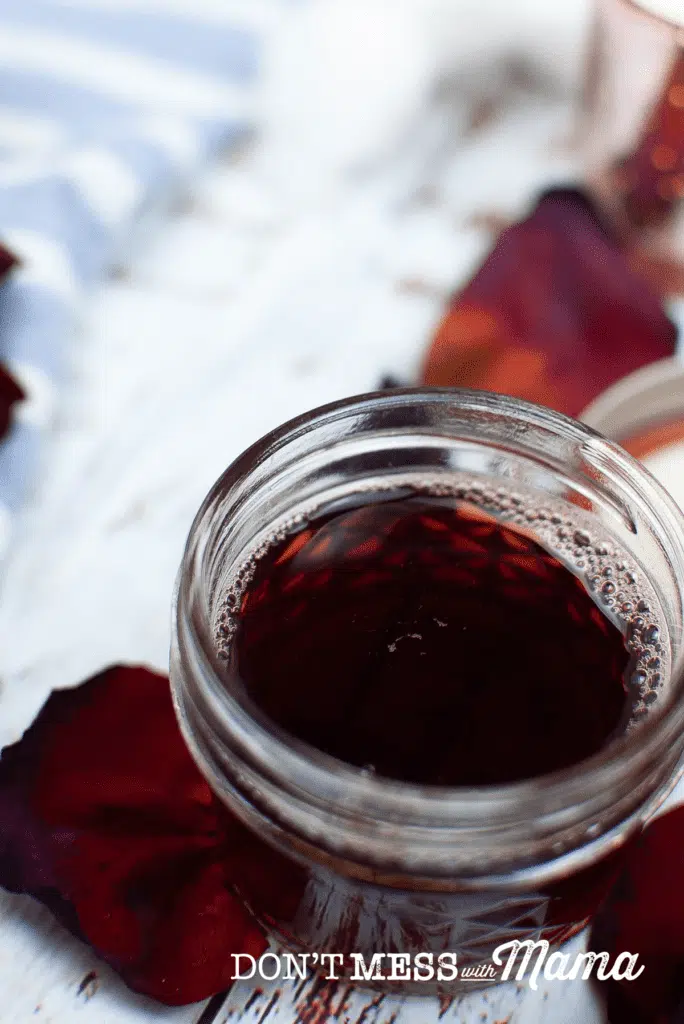 glass jar with dark red toner and rose petals