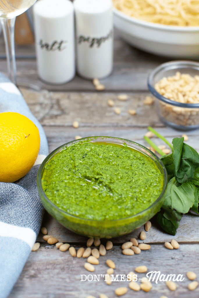 glass bowl of basil pesto with lemon, basil and salt and pepper shakers in background