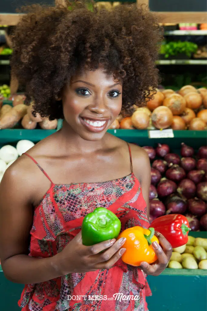 African-American woman holding bell peppers and smiling at a grocery store
