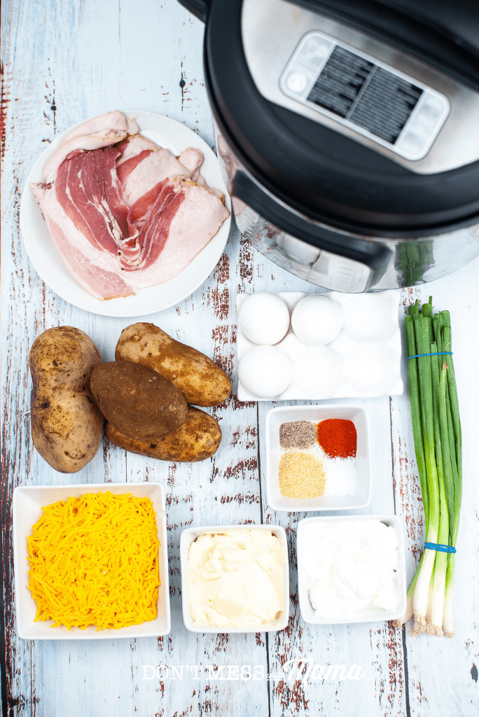 overview photo of ingredients to make baked potato salad like potatoes, bacon, cheese, spices, eggs, green onions on a table next to an Instant Pot
