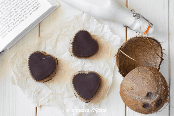 almond butter cups on parchment paper on a table with milk and coconut shells