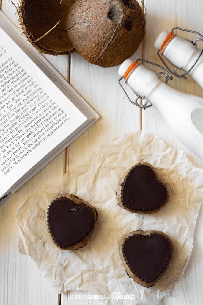 homemade almond butter cups on parchment paper on a table with milk and coconuts nearby