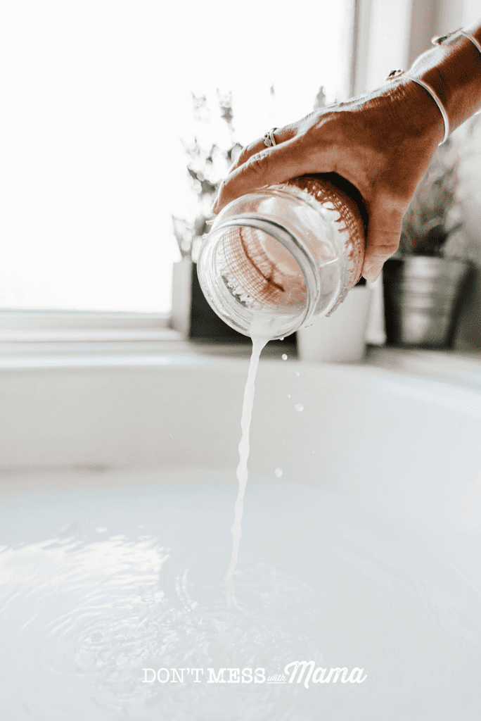 hand pouring jar of bubble bath into bath tub